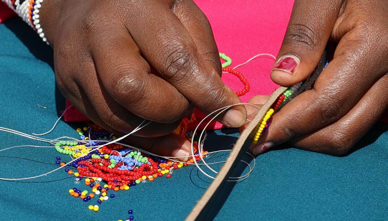 Hands threading glass beads onto leather